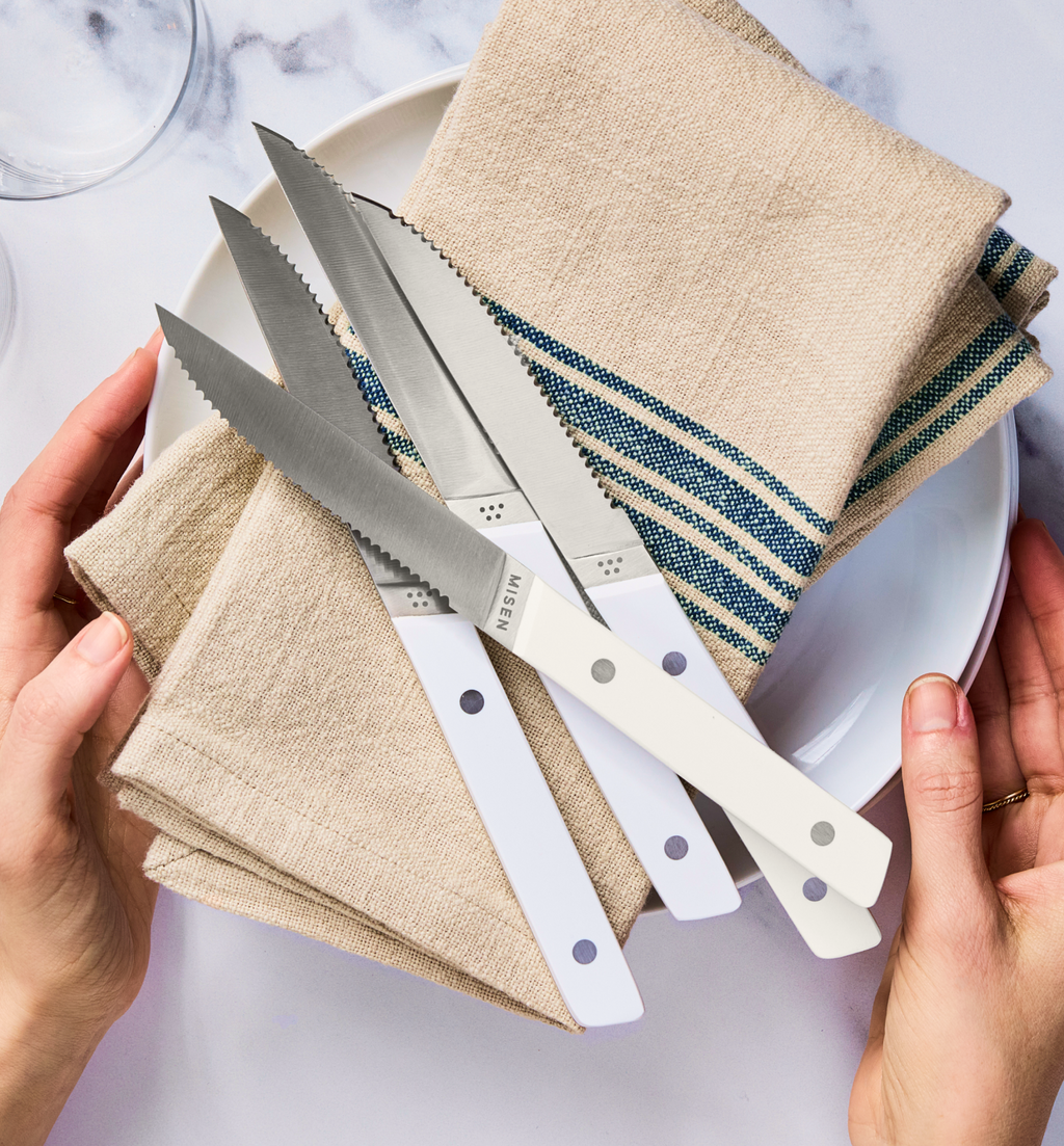 Misen steak knives with white handles displayed on linen napkins and white plate